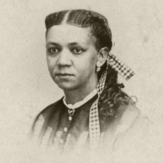 Black and white headshot photo of Fanny Jackson Coppin with hair braided with gingham ribbon while also wearing a button up blouse